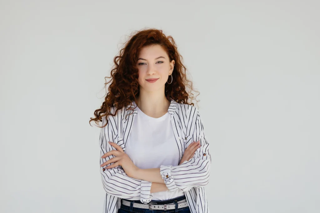 Pretty young redhead lady standing isolated over white wall background With Arms Crossed
