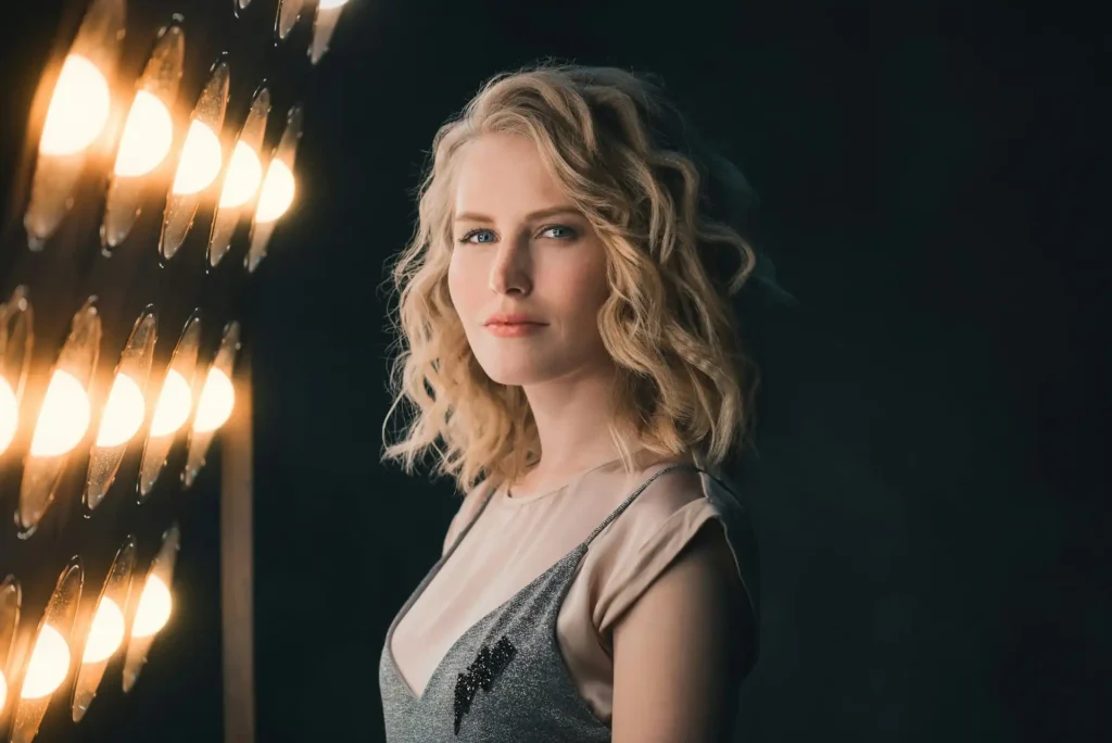 A beautiful blonde woman posing in front of a series of bright, warm studio lights.