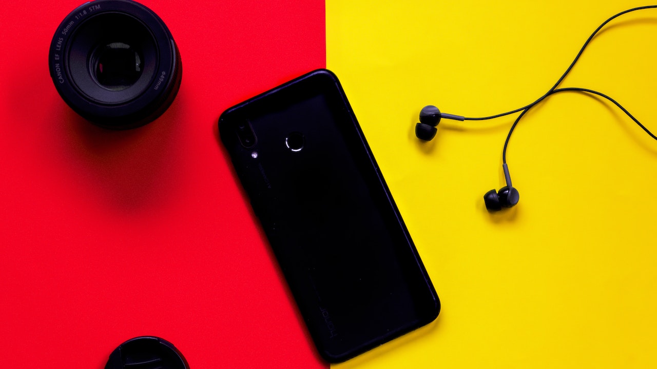 Black Smartphone Besides Earphones and Camera Lens